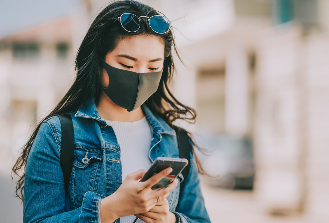 Woman with mask on looking at her phone while walking outdoors